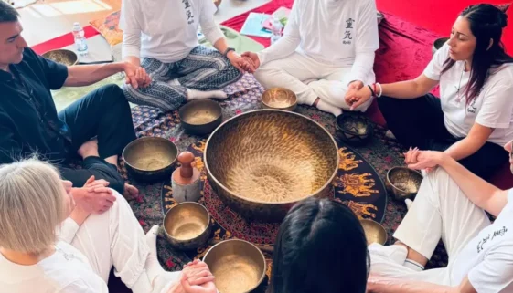 Cerimonia di gruppo per il corso reiki secondo livello: praticanti siedono in cerchio con campane e strumenti intorno, mani unite in meditazione.