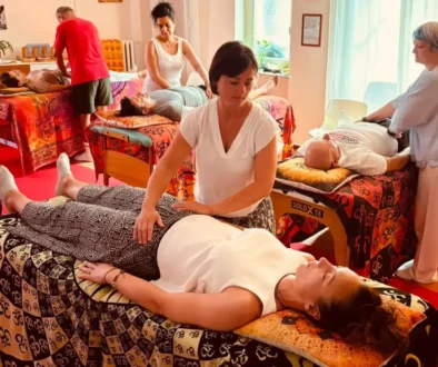 Donna distesa sul lettino, mentre operatore appoggia le mani sul corpo; varie persone ricevendo trattamenti in una sala colorata, ampi lettini e massaggiatori. come funziona il reiki.