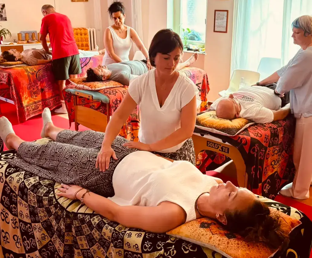Donna distesa sul lettino, mentre operatore appoggia le mani sul corpo; varie persone ricevendo trattamenti in una sala colorata, ampi lettini e massaggiatori. come funziona il reiki.