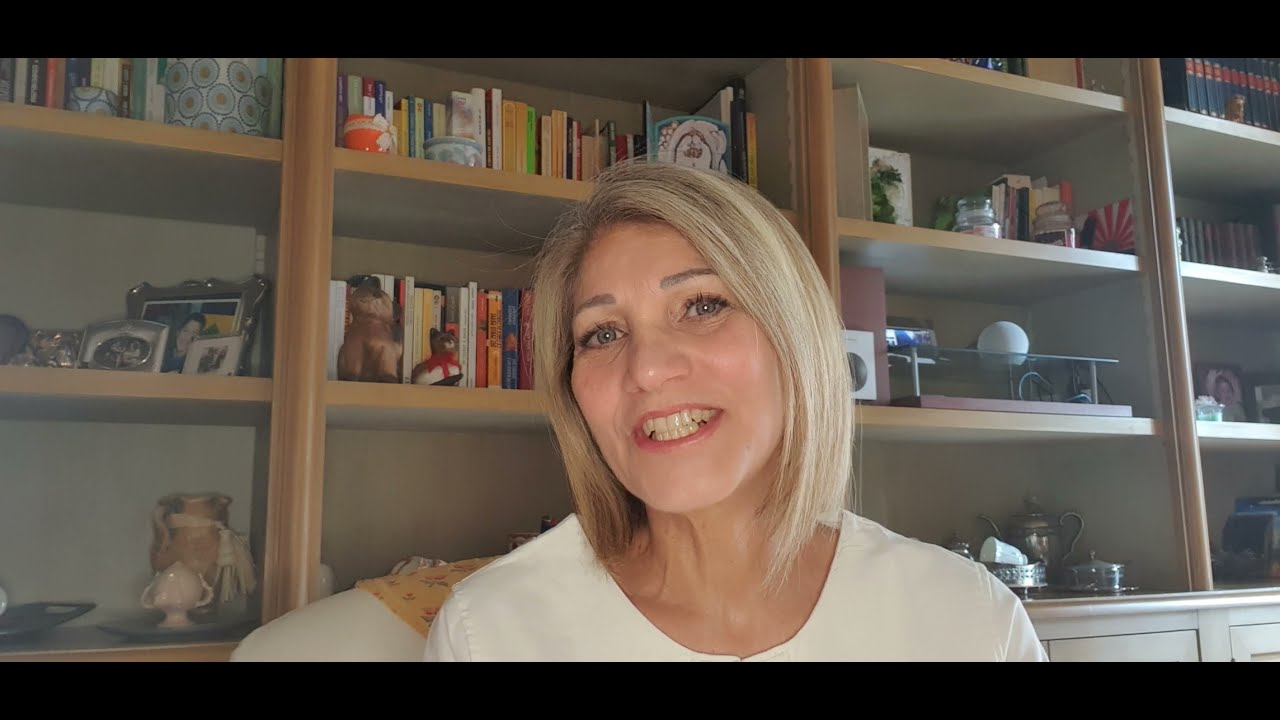 Donna sorridente in soggiorno con mensole piene di libri sullo sfondo, pronta a spiegare reiki cos'è.