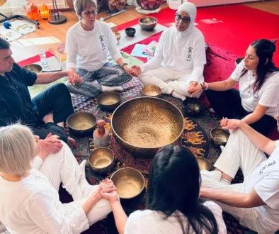 Gruppo di persone sedute in cerchio su tappeto, con strumenti rituali al centro durante una sessione di meditazione Reiki, indossano abiti bianchi.